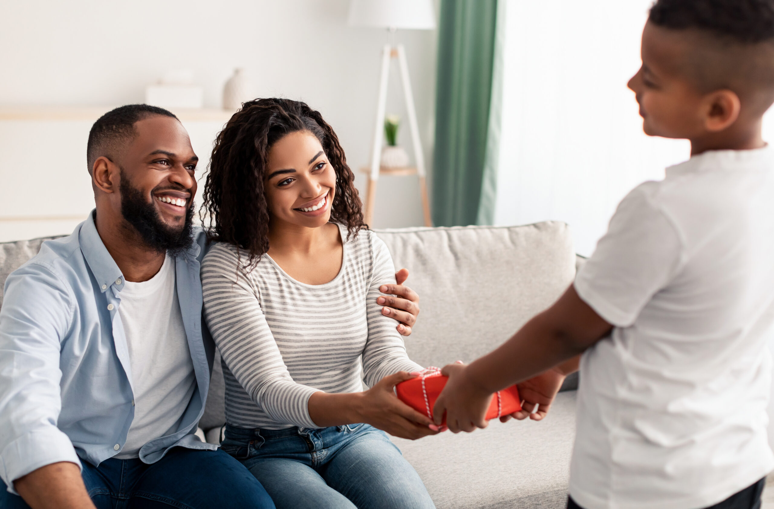 young boy hands his mother her mothers day gift while his father smiles
